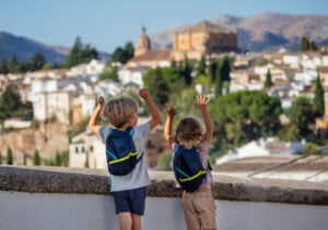 Kids stand on hill and lift hands next to panorama of Ronda, Spain